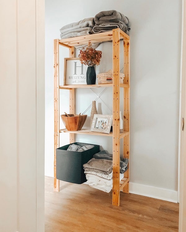 Wooden bathroom storage rack with towels, baskets, decor, and a vase on display.