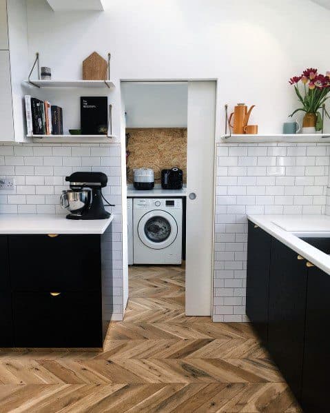 Modern kitchen with herringbone hardwood flooring, black cabinetry, and subway tile backsplash, featuring a door leading to a laundry area