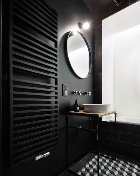 Luxurious black bathroom with a heated towel rack, round mirror, and geometric floor tiles.