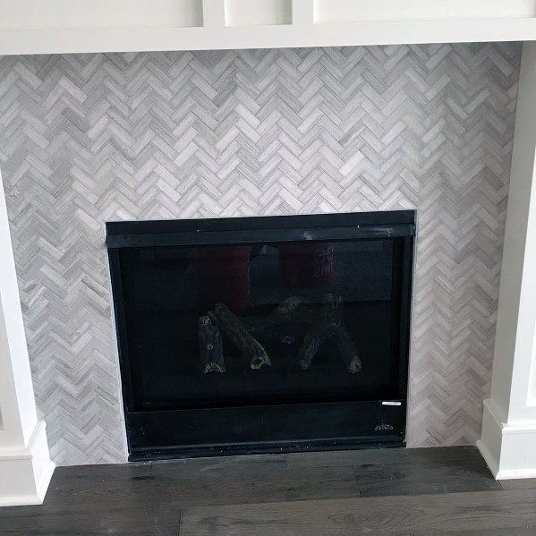 Fireplace with gray herringbone tile surround and a black gas insert.