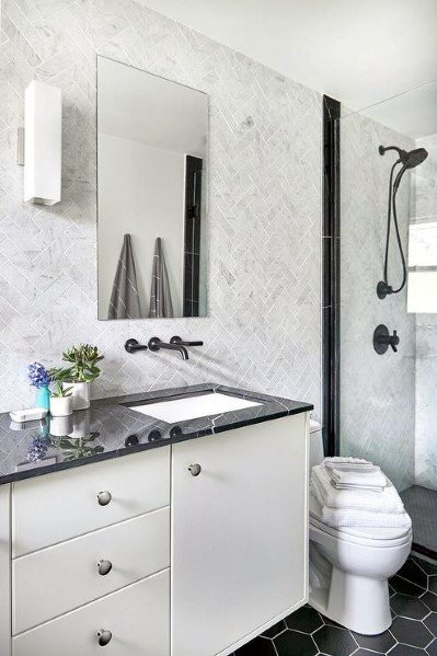 Modern bathroom with white vanity, black countertop, herringbone backsplash, and black hexagon tile floor.