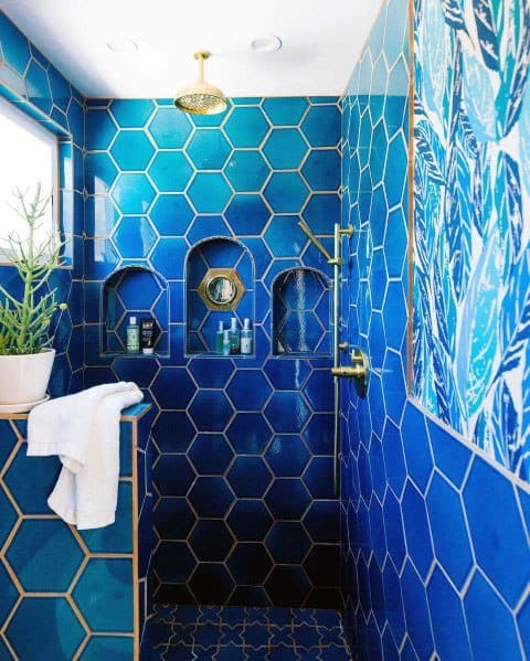 Bathroom with bold blue hexagon tiles, gold grout, built-in shelves, and gold shower fixtures.