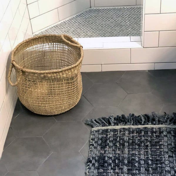 Modern bathroom with hexagon grey floor tiles, a woven basket, and a textured rug near a tiled shower