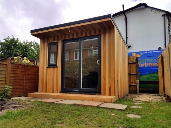 Wooden backyard shed with a slanted roof and glass sliding doors in a small garden.