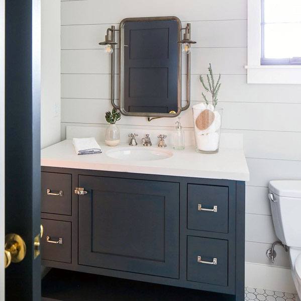 Bathroom with dark vanity, round mirror, white shiplap walls, and decorative items on the countertop