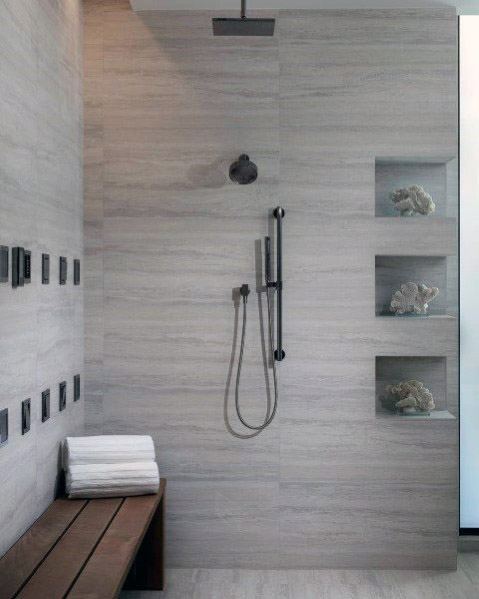 Contemporary shower with grey tile walls, black fixtures, built-in shelving with decorative items, and a wooden bench