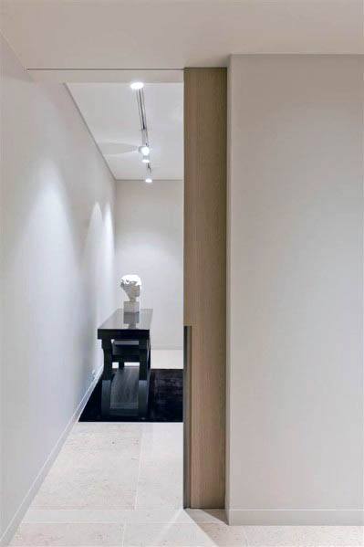 Minimalist wood pocket door leads to a sleek hallway with neutral tones, recessed lighting, and a modern black console table