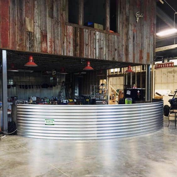 Industrial garage bar with curved corrugated metal counter, reclaimed wood accents, and red lighting.