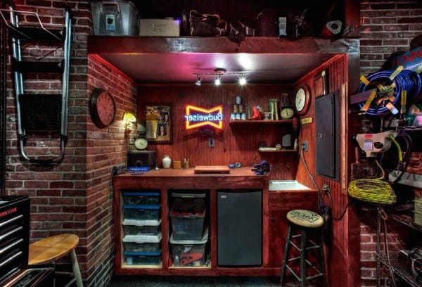 Compact garage bar with brick walls, wooden cabinetry, Budweiser neon sign, and storage shelves.