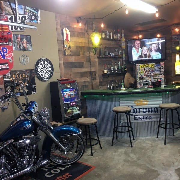 Garage bar with corrugated metal counter, motorcycle decor, dartboard, and wooden shelving.