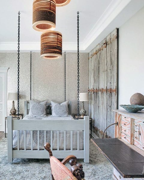 Rustic bedroom with gray bed suspended by chains and reclaimed wood decor.