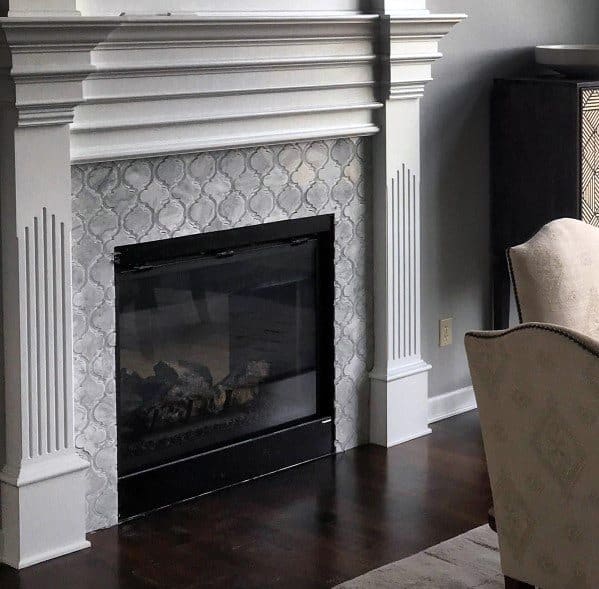 A sophisticated fireplace with intricate patterned tiles in soft gray tones, framed by a traditional white mantle.