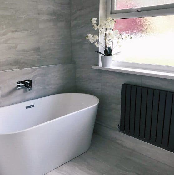 Modern bathroom with a freestanding tub, grey tiles, and a window with potted orchids