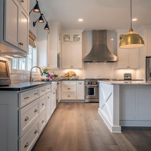 Charming kitchen with light hardwood flooring, white cabinetry, a sleek range hood, and stylish gold pendant lighting