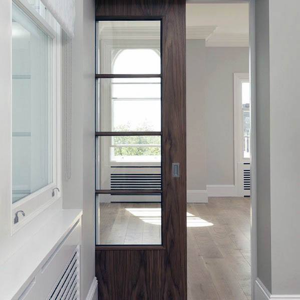 Modern wood pocket door with glass panels and black trim opens to a bright room featuring arched windows and hardwood flooring