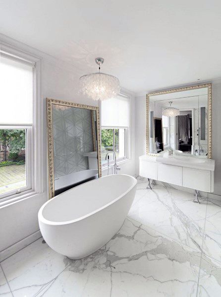 Luxurious white bathroom with a freestanding tub, large mirrors, chandelier, and marble flooring