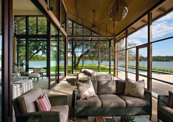 A luxurious sunroom with floor-to-ceiling glass walls, cushioned wicker sofas, and a serene outdoor view.