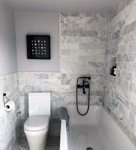 Modern bathroom with white marble tiles, a bathtub, wall-mounted shower, toilet, and framed art on the wall