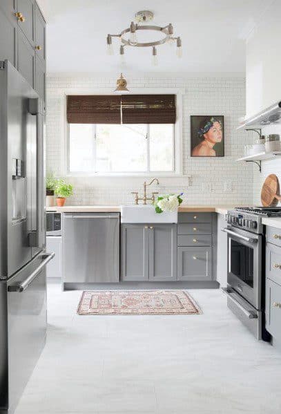 Stylish kitchen with grey cabinetry, marble-look flooring, modern appliances, and a cozy rug, featuring natural light and artwork