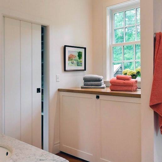 White pocket door in a bright bathroom featuring wooden countertops, folded towels, and a large window with a garden view