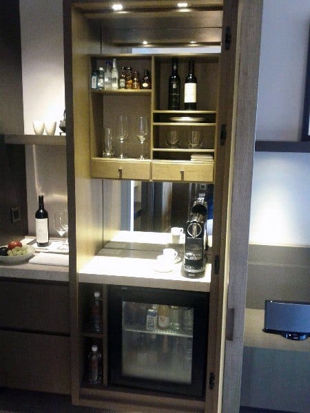 Compact wooden mini bar with shelves, wine storage, glassware, and built-in mini fridge.