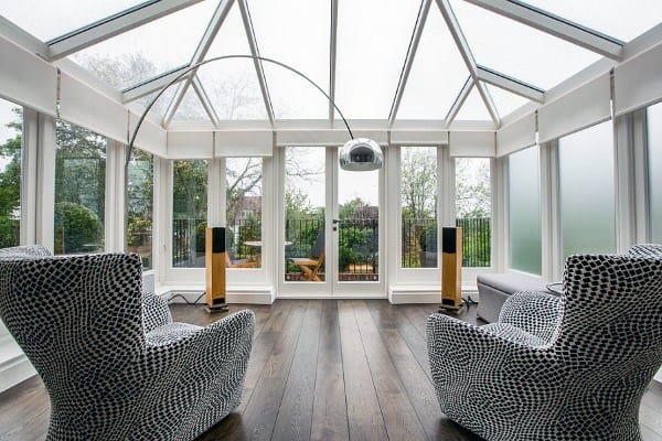 Modern sunroom with geometric-patterned armchairs, hardwood flooring, and a sleek glass ceiling.