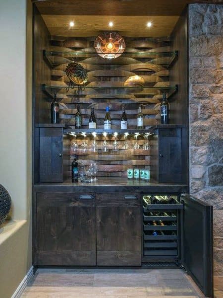 Rustic mini bar with wood shelves, wine fridge, stone wall accents, and warm lighting.