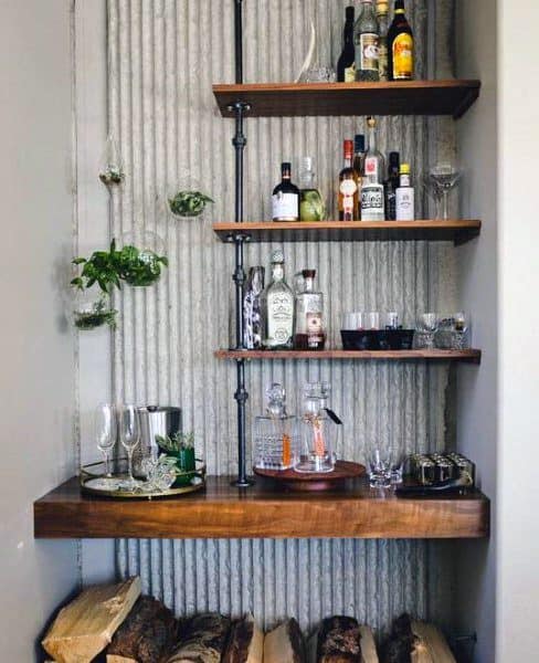 Rustic mini bar with wood shelves, industrial pipe supports, and textured wall backdrop.