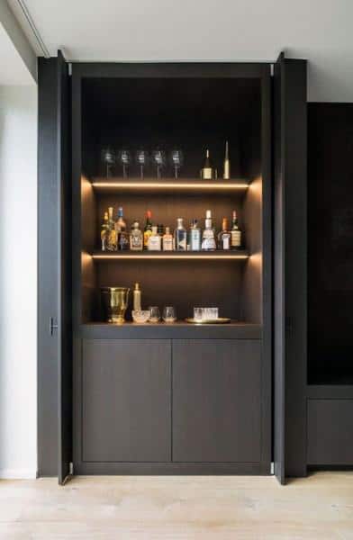 Minimalist mini bar with dark cabinets, illuminated shelves, and elegant liquor display.