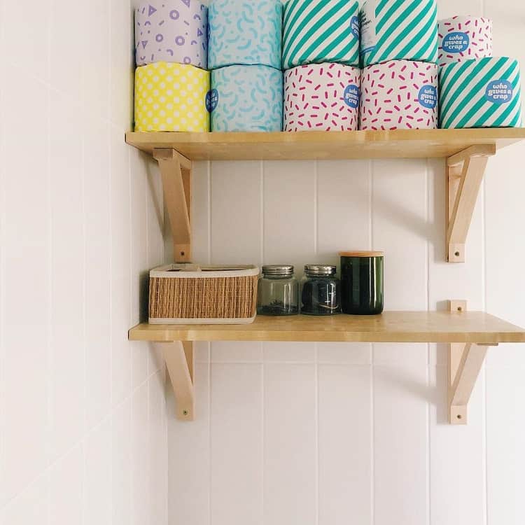 Wooden bathroom shelves with colorful toilet paper, storage basket, and jars.