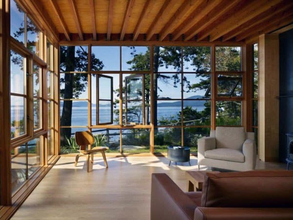 Sunroom with wood ceiling, floor-to-ceiling windows, scenic lake view, and cozy seating.