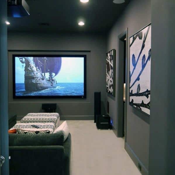 Compact home theater with grey walls, cozy seating, large screen, and abstract wall art.