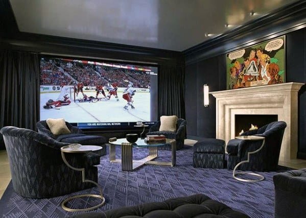 Home theater room with dark blue walls, plush chairs, large screen, and fireplace with mantel.