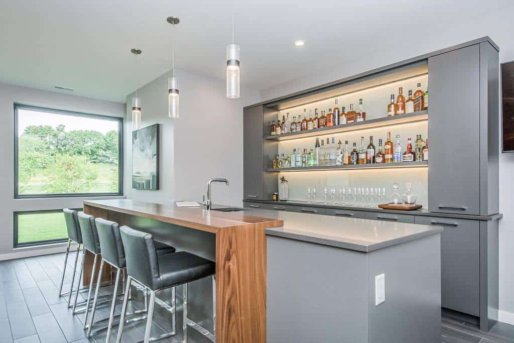 Modern wet bar with sleek gray cabinetry, illuminated shelves, wood island, and pendant lighting.