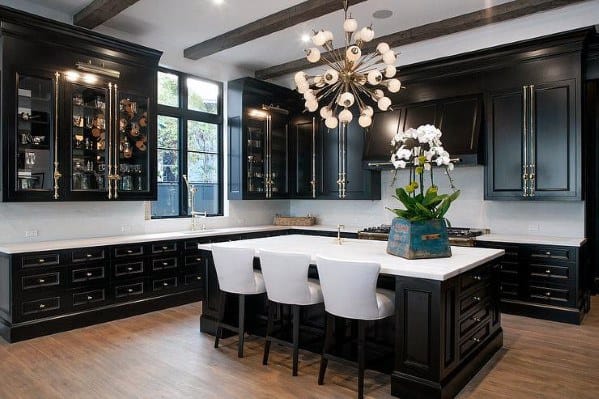 Luxurious black kitchen cabinets with glass displays, white countertops, and a statement chandelier.