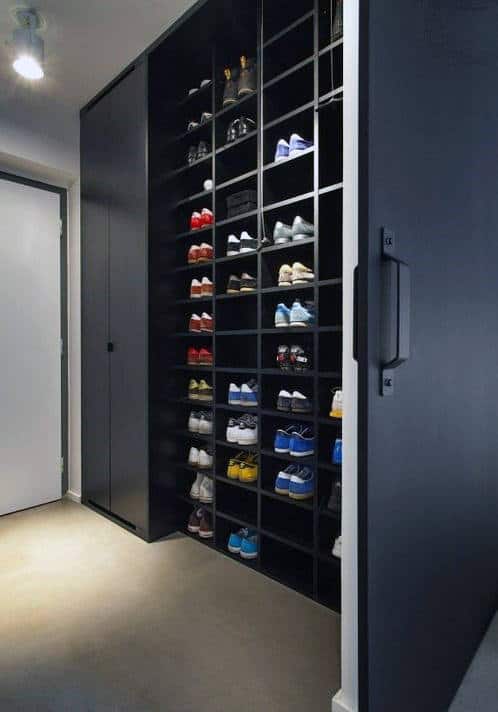 A neatly arranged shoe closet with black shelves holding various colorful sneakers