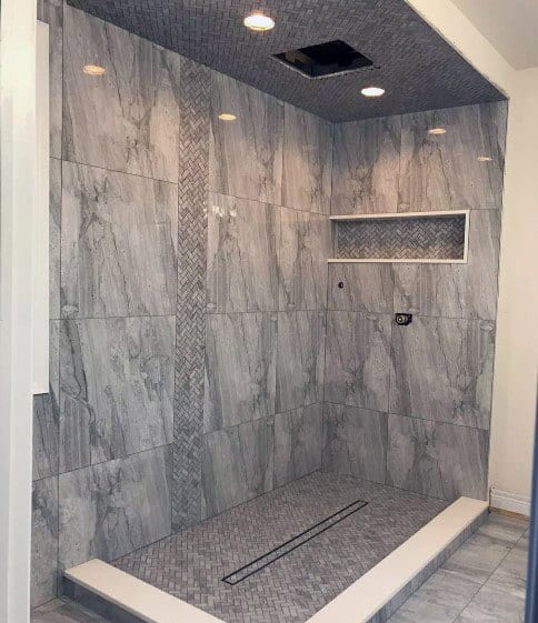 A grey tiled shower with a built-in shelf and ceiling lights