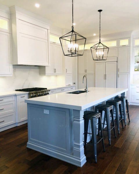 Elegant kitchen with black lantern-style pendant lights above a white marble island, complemented by metal bar stools and light cabinetry