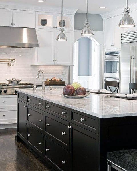 Black kitchen island with marble countertop, white cabinets, and pendant lighting.