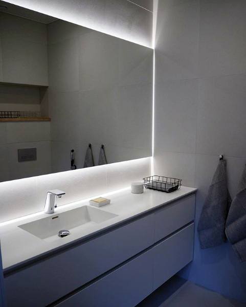 Modern bathroom with illuminated mirror, white sink, and towels hanging on the wall