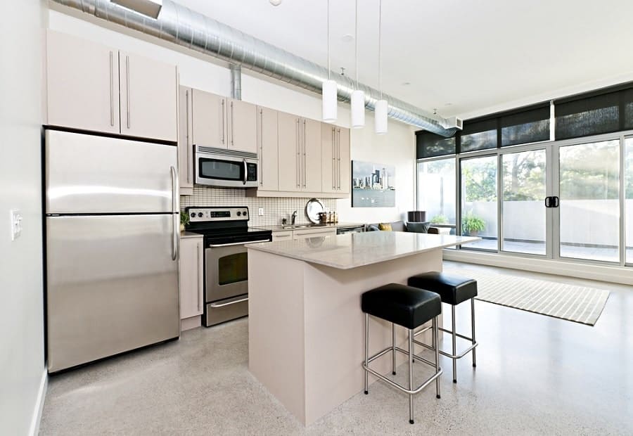 Modern kitchen with stainless steel appliances, white cabinets, island stools, and expansive windows