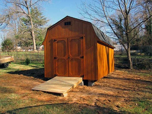 Barn-style wooden shed with double doors and a small ramp, situated in a spacious backyard.