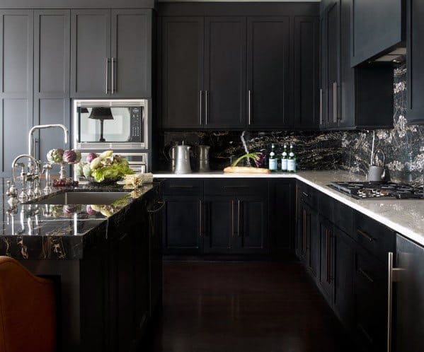 Black kitchen cabinets with dark marble countertops, reflective backsplash, and modern fixtures.