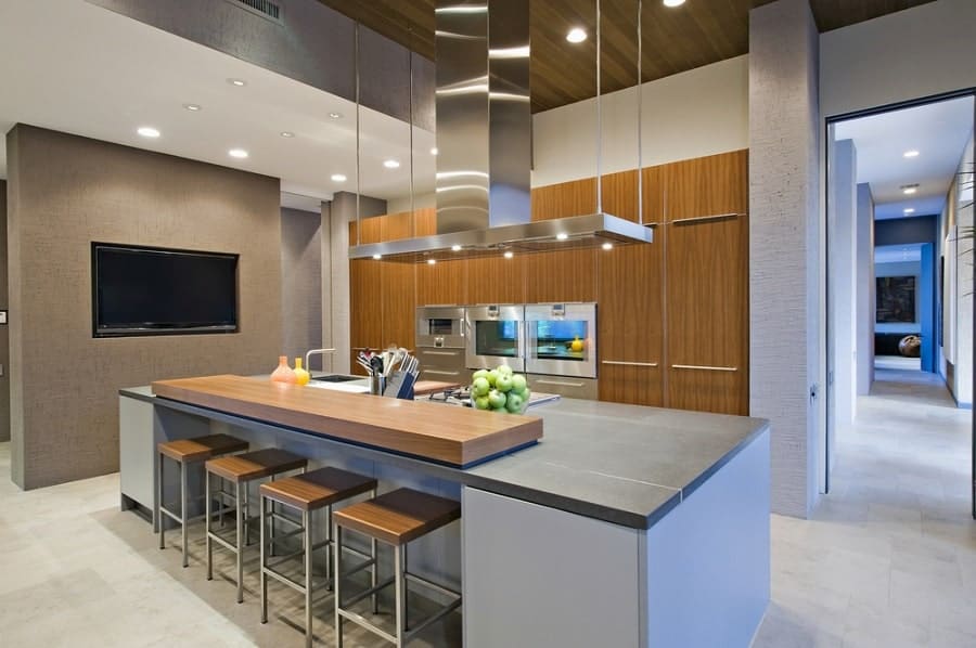 Modern kitchen featuring a stunning central island, bar stools, wooden cabinets, wall-mounted TV, and stainless appliances