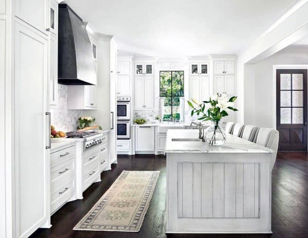 Elegant kitchen with dark hardwood flooring, white cabinetry, marble countertops, and a modern black range hood, complemented by a decorative rug