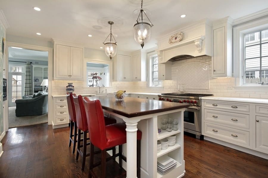 A modern kitchen featuring a wooden island, red chairs, and white cabinetry with stylish pendant lights