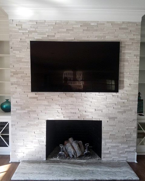 A white stacked stone fireplace with a sleek TV mounted above and a cozy wood-burning hearth below.