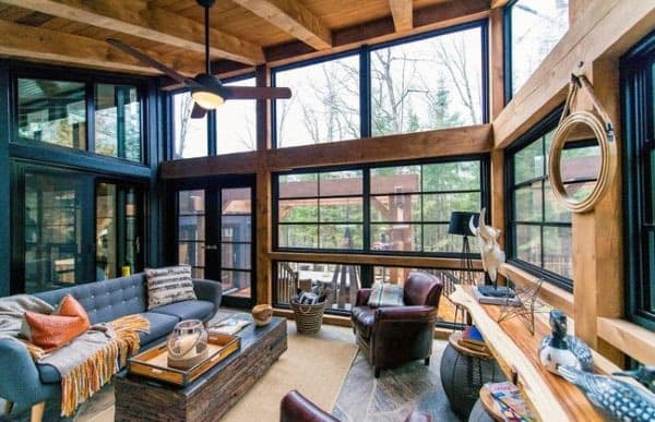 Rustic sunroom with wood beams, black windows, and cozy leather seating.