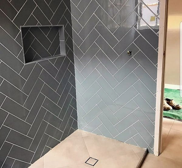 Grey herringbone patterned shower tiles with recessed shelf and beige floor tiles