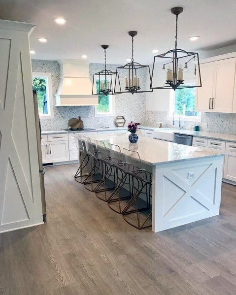 Modern kitchen with light wood flooring, white cabinetry, a large island with stylish gold bar stools, and elegant pendant lighting